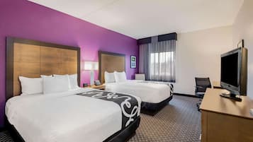 A hotel room with two beds, a desk with a TV, and a window with curtains.