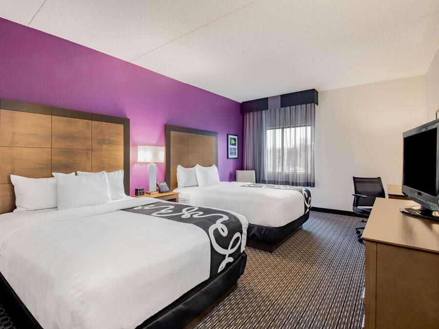 Una habitación de hotel con dos camas, un escritorio con televisor y una ventana con cortinas.