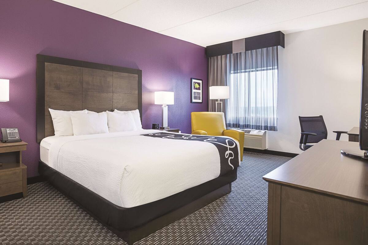A hotel room with a large bed, a desk, a chair, and a window with curtains.