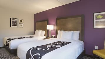 A hotel room with two beds, a nightstand with a lamp, and a small table.