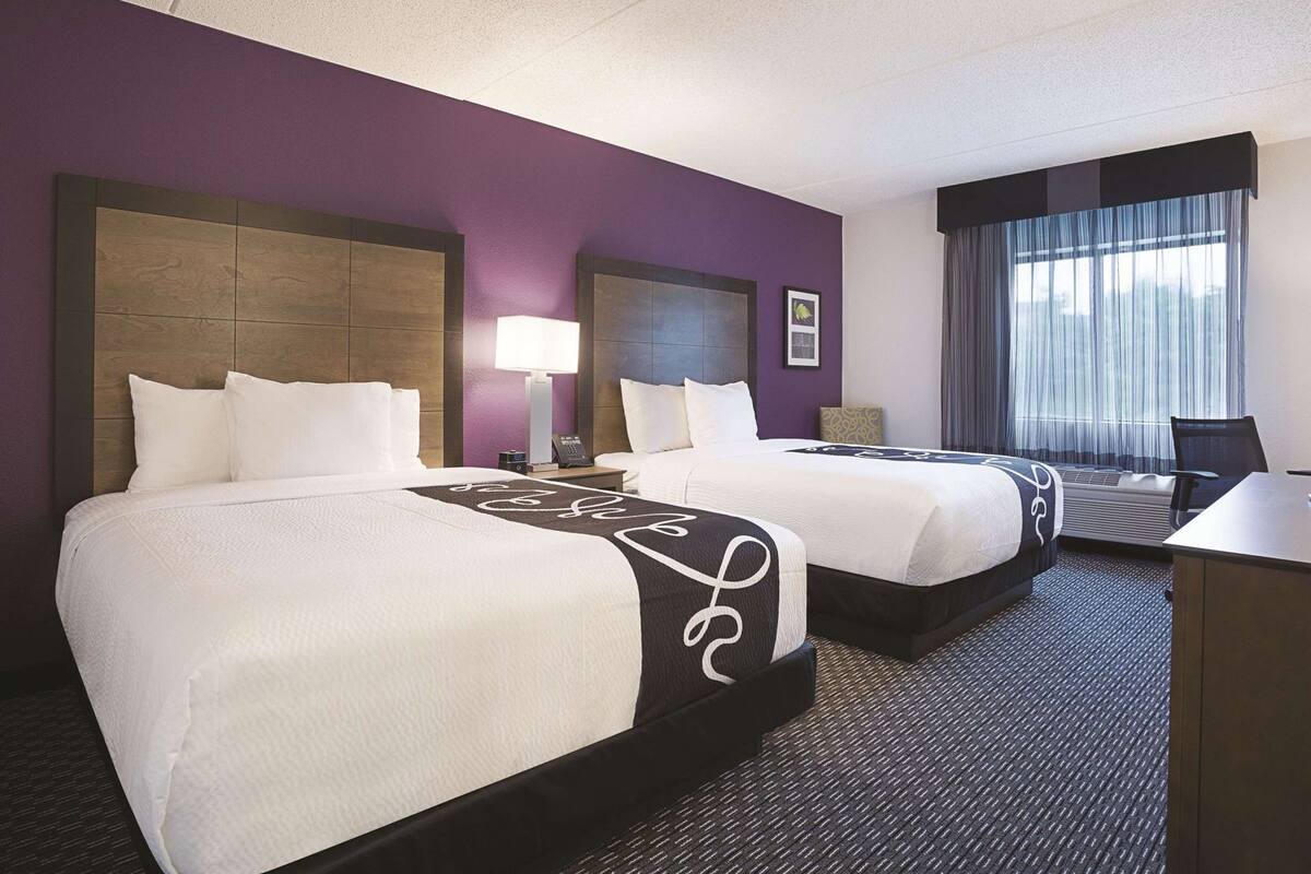 A hotel room with two beds, a desk, and a window with curtains.