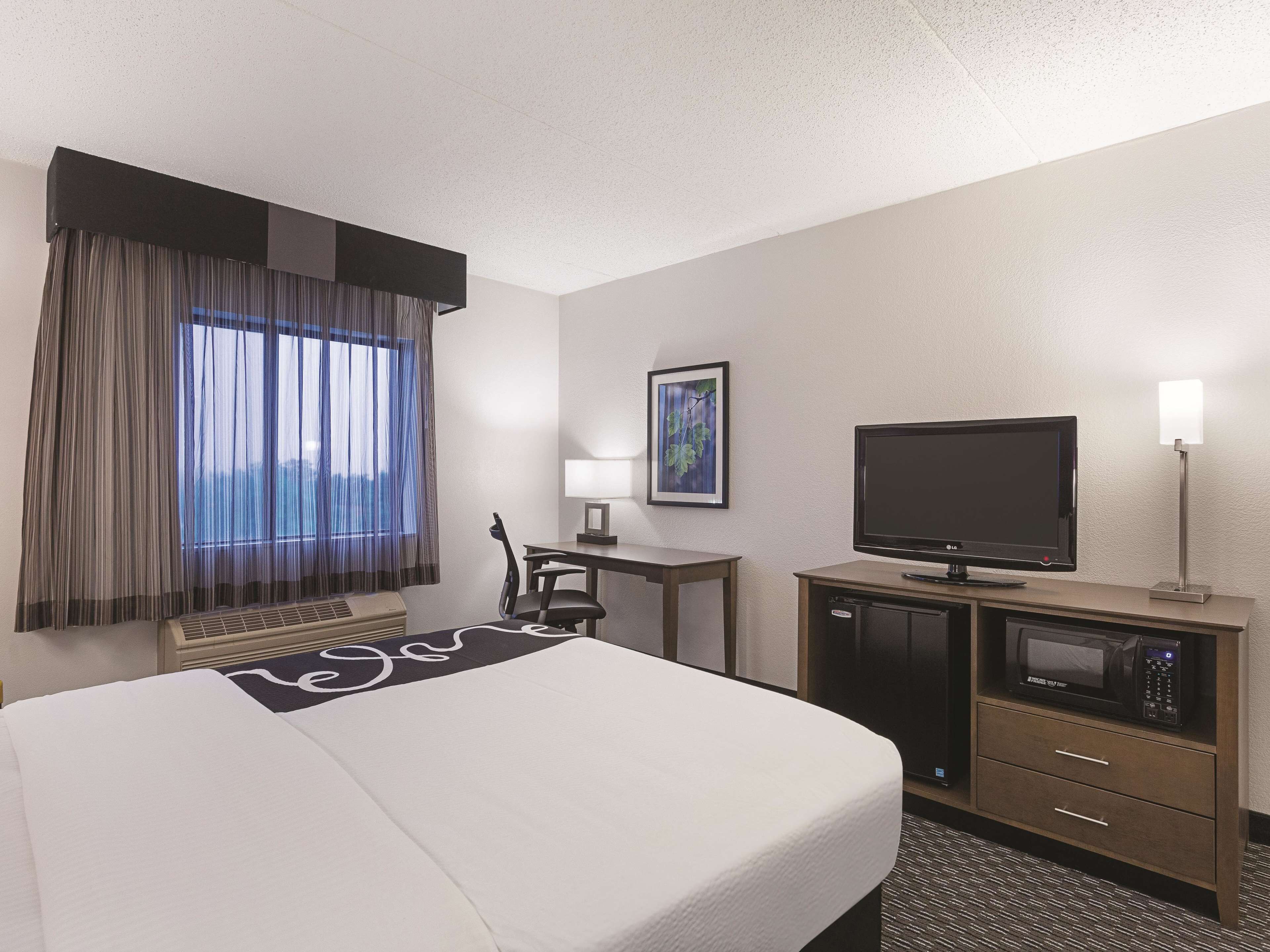 A hotel room with a bed, a desk, a television, a microwave, and a window with curtains.