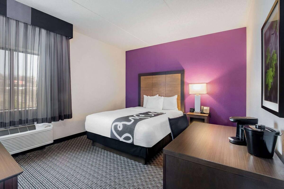 A hotel room with a bed, a desk, a lamp, and a window with curtains.