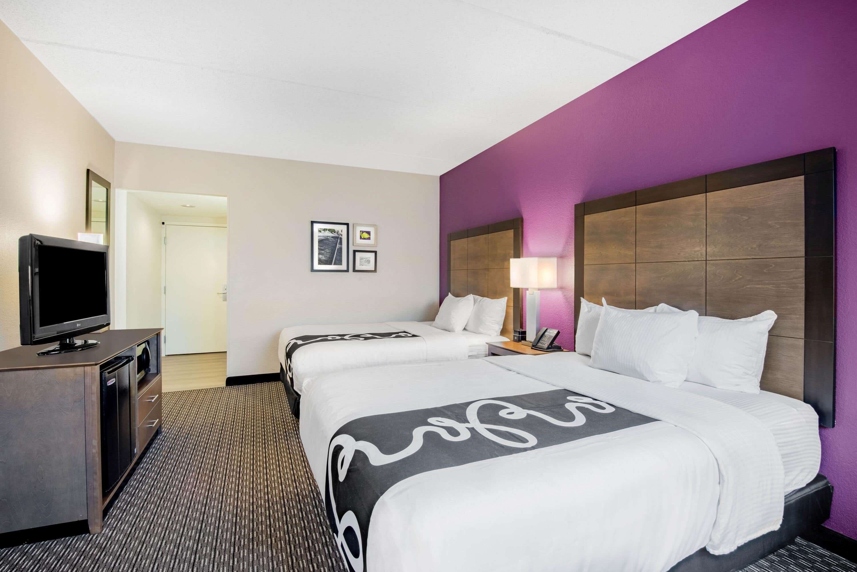 A hotel room with two beds, a TV, a desk, and a lamp.