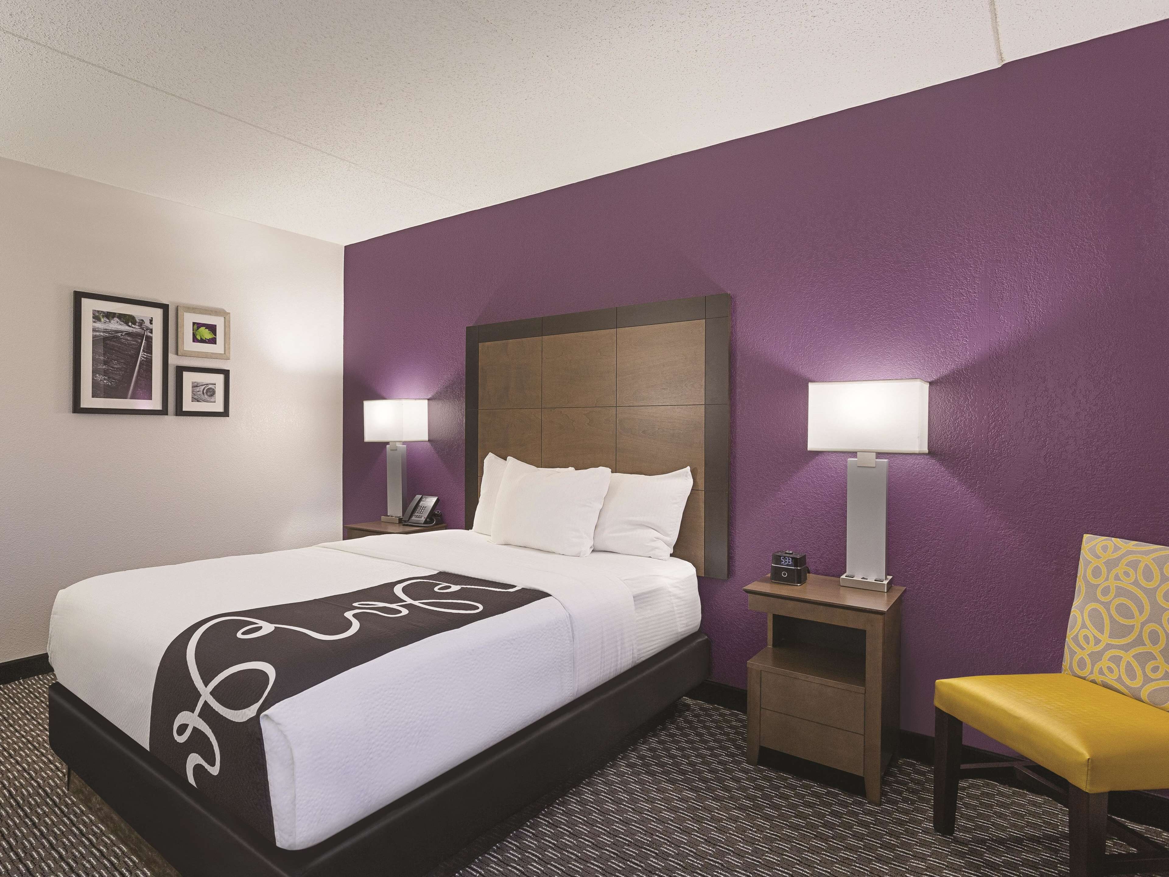 Una habitación de hotel con una cama, dos mesitas de noche con lámparas, una silla y una pared decorada con cuadros.