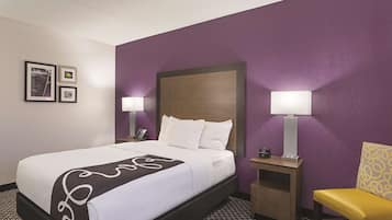 Una habitación de hotel con una cama, dos mesitas de noche con lámparas, una silla y una pared decorada con cuadros.