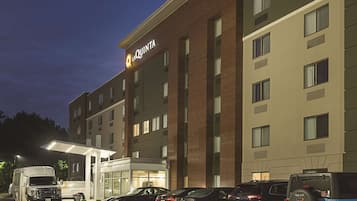 A hotel with a modern design, featuring a prominent sign and a parking lot with several cars and a service truck.