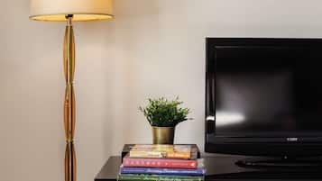 A black TV on a wooden cabinet with a black stand, a lamp with a gold base, and a small plant in a gold pot.