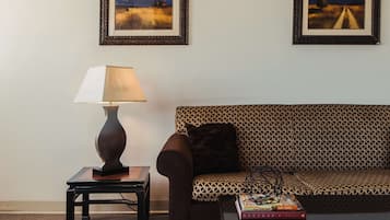 Un salón con un sofá, una mesita de noche con una lámpara y dos cuadros en la pared.