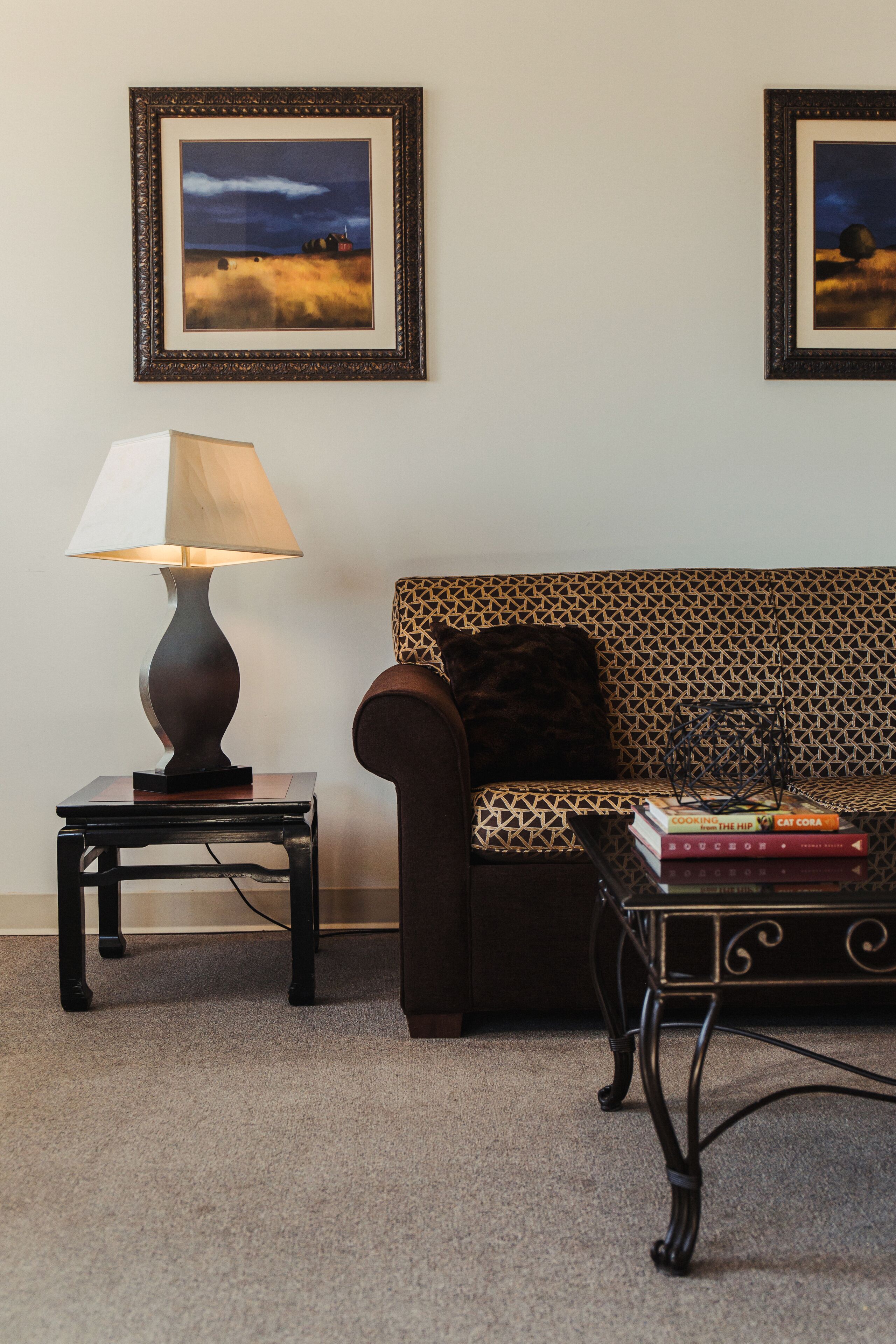 A room with a sofa, a table with a lamp, and two framed pictures on the wall.