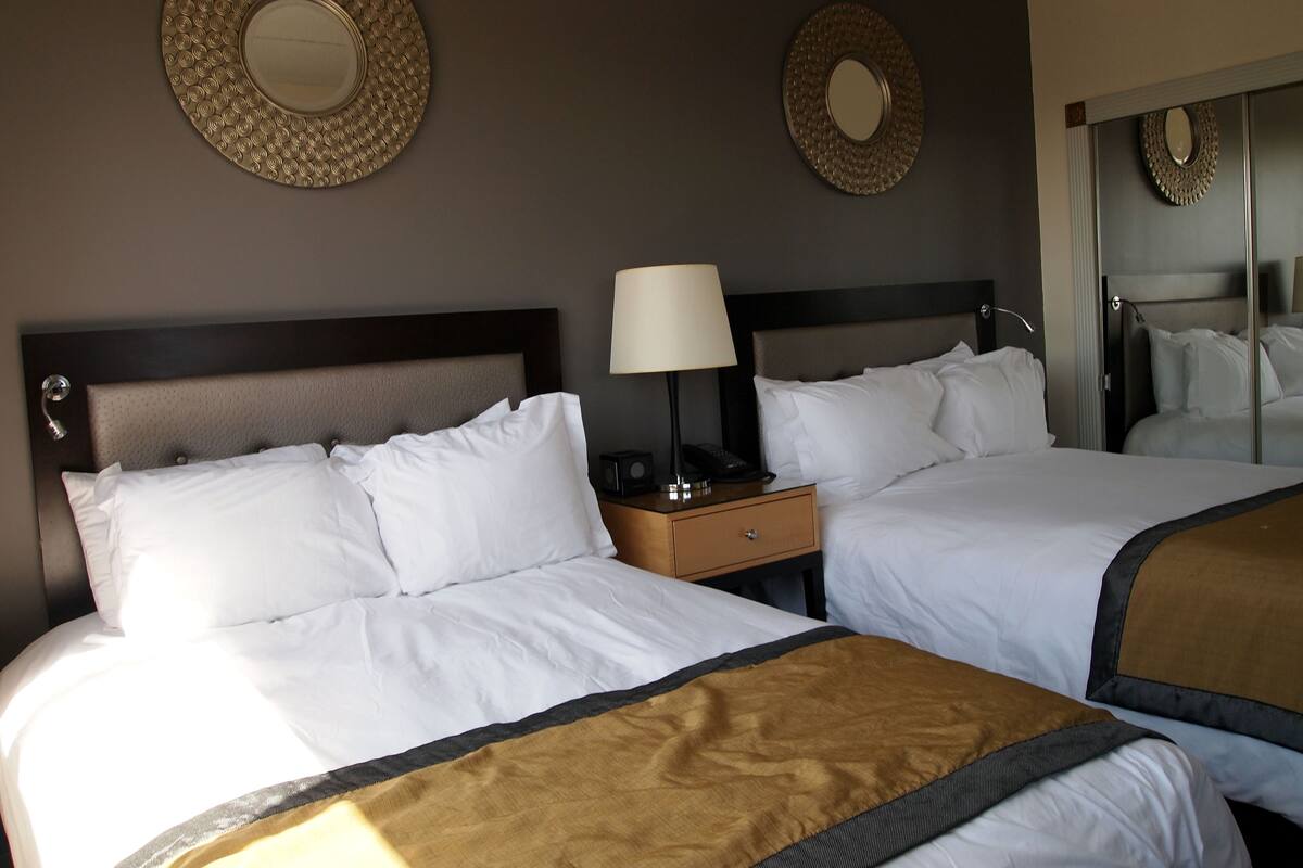 A hotel room with two beds, a nightstand with a lamp, and two wall mirrors.