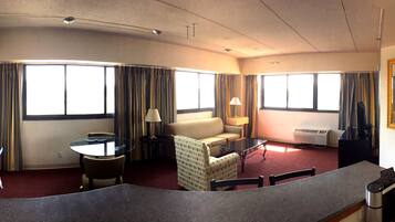 A hotel room with a sofa, a glass table, a chair, a lamp, and a large window with curtains.