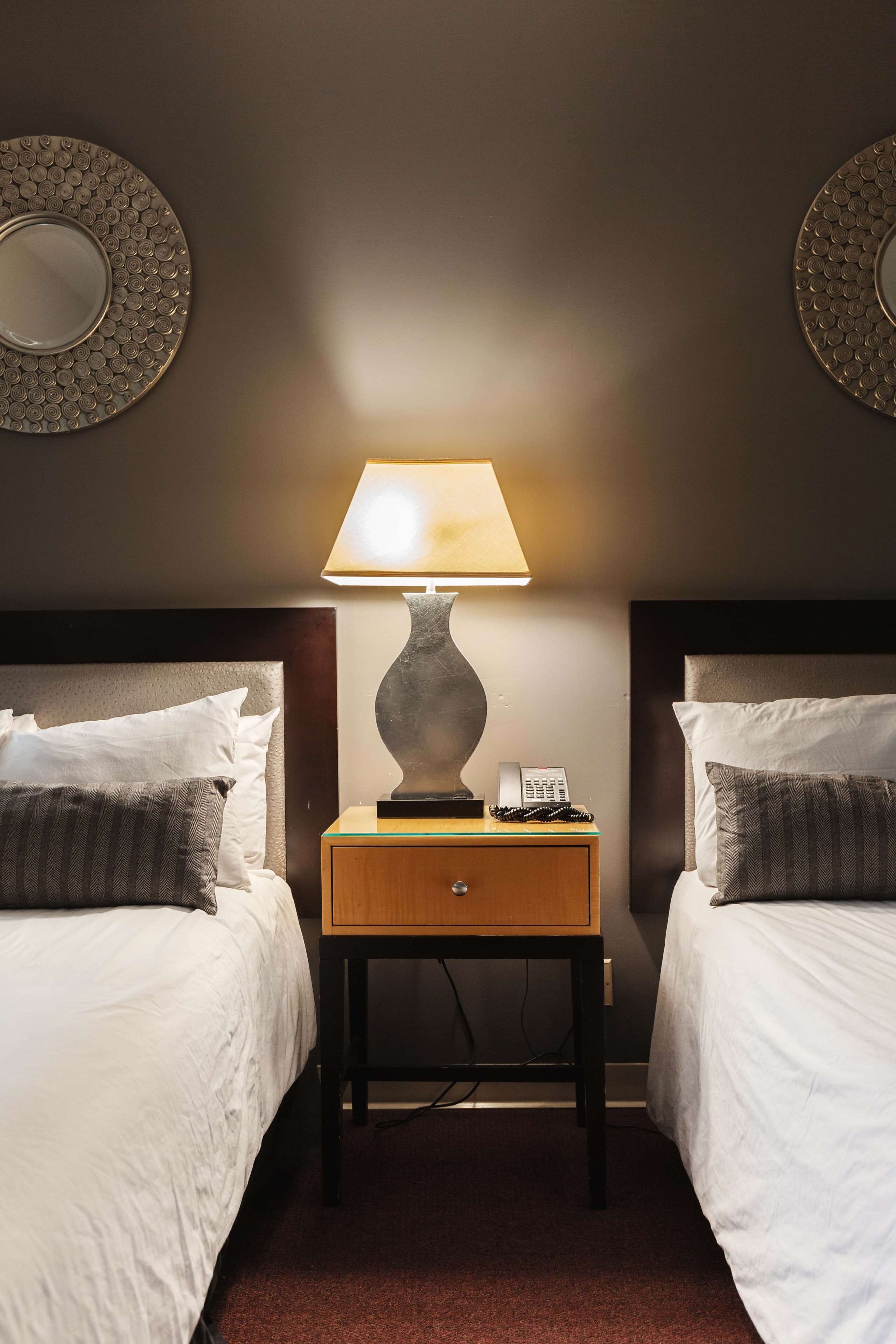 Habitación de hotel con dos camas, una mesita de noche con lámpara, teléfono y espejo en la pared.