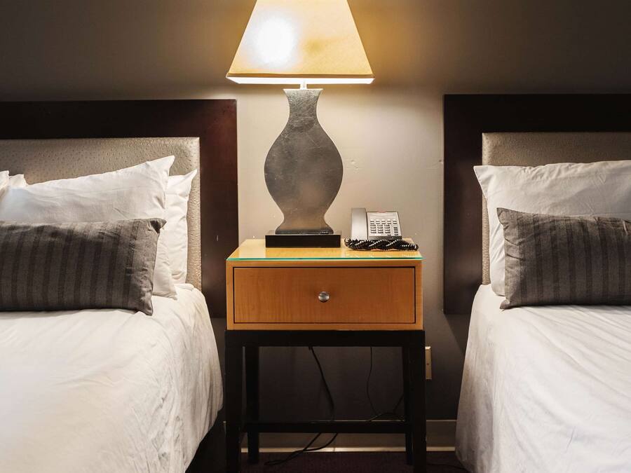 Habitación de hotel con dos camas, una mesita de noche con lámpara, teléfono y espejo en la pared.