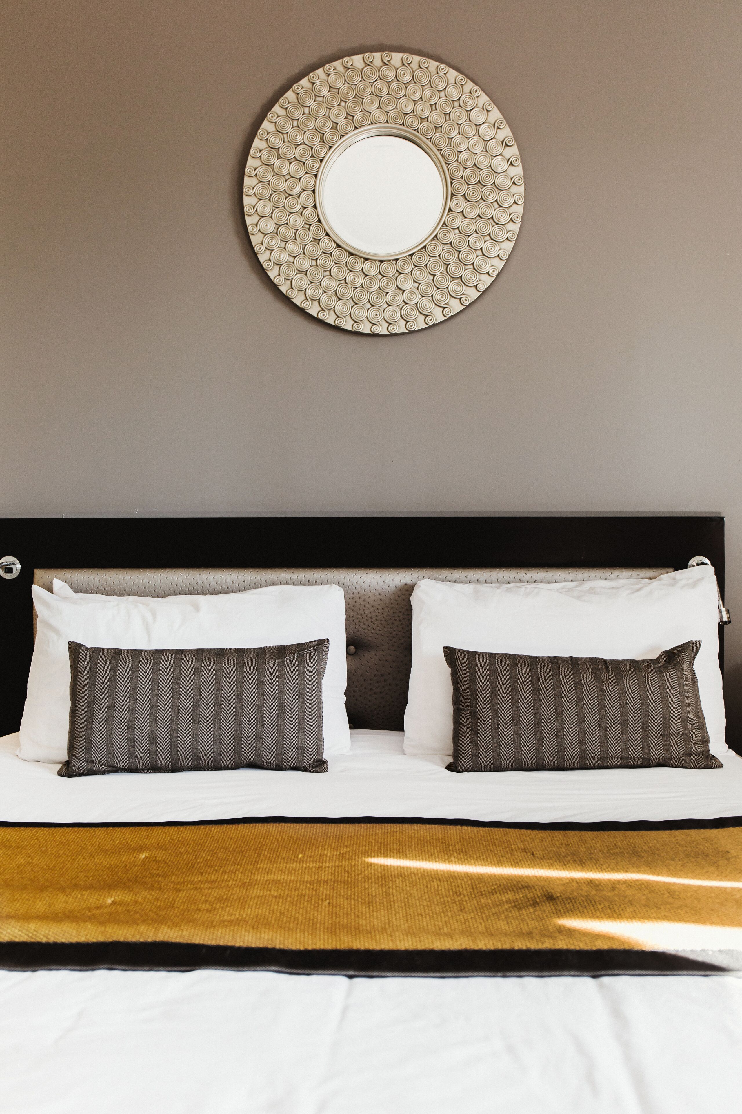 A neatly made bed with two pillows, a headboard, and a circular wall decoration above it.