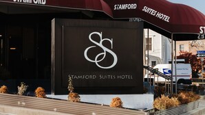 L’entrée de l’hôtel Stamford Suites offre une vue dégagée sur la façade de l’immeuble, avec une grande enseigne et un espace de stationnement.