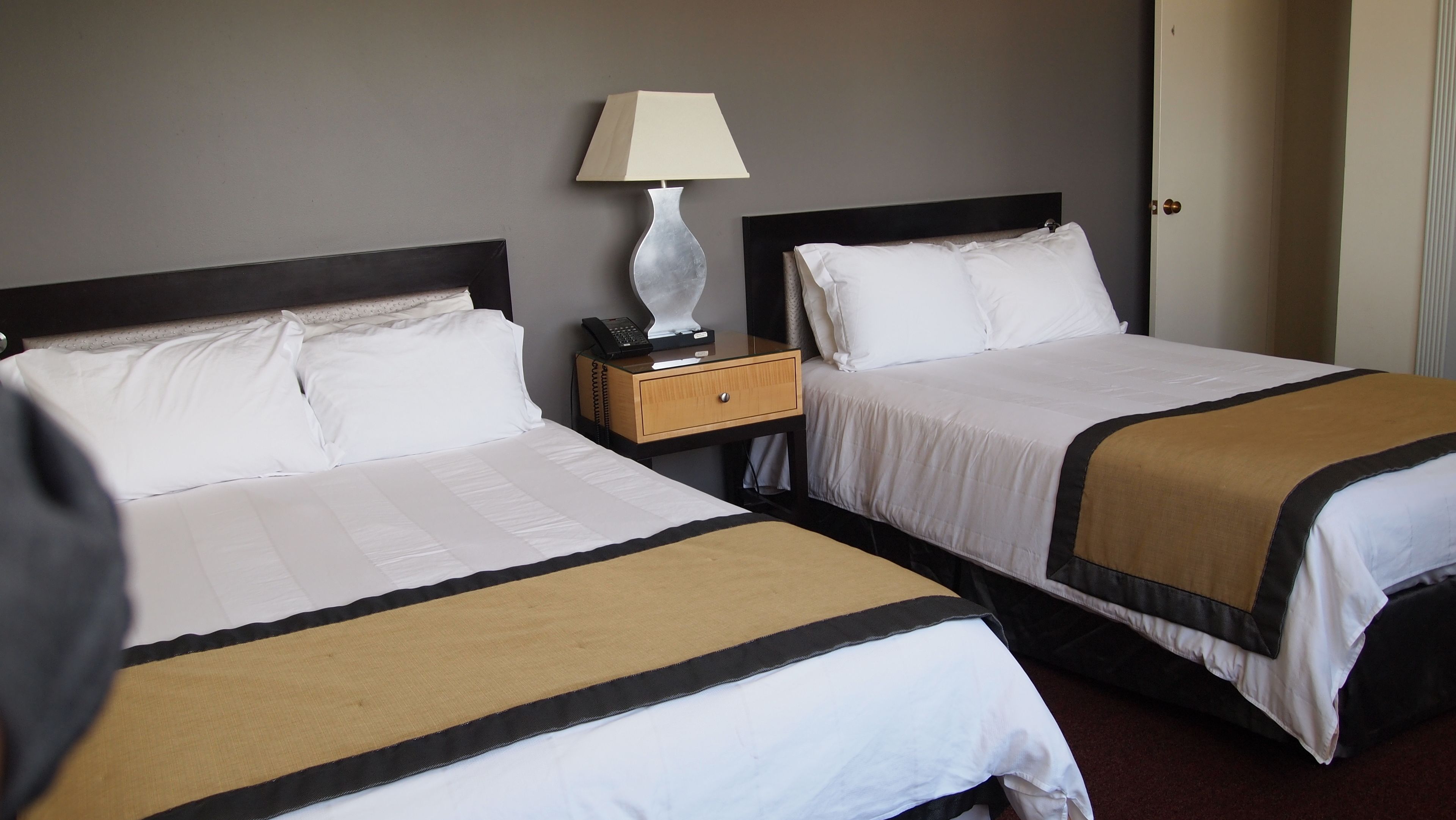 Habitación de hotel con dos camas, una mesita de noche, una lámpara y una puerta.