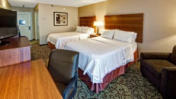 A hotel room with two beds, a desk with a television, a chair, and a patterned carpet.