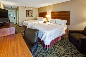 Habitación de hotel con dos camas, un escritorio con televisión, una silla y una alfombra estampada.