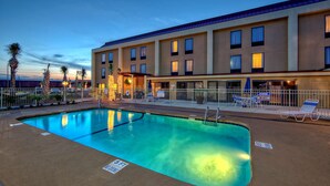 A hotel with a swimming pool, lounge chairs, and palm trees.