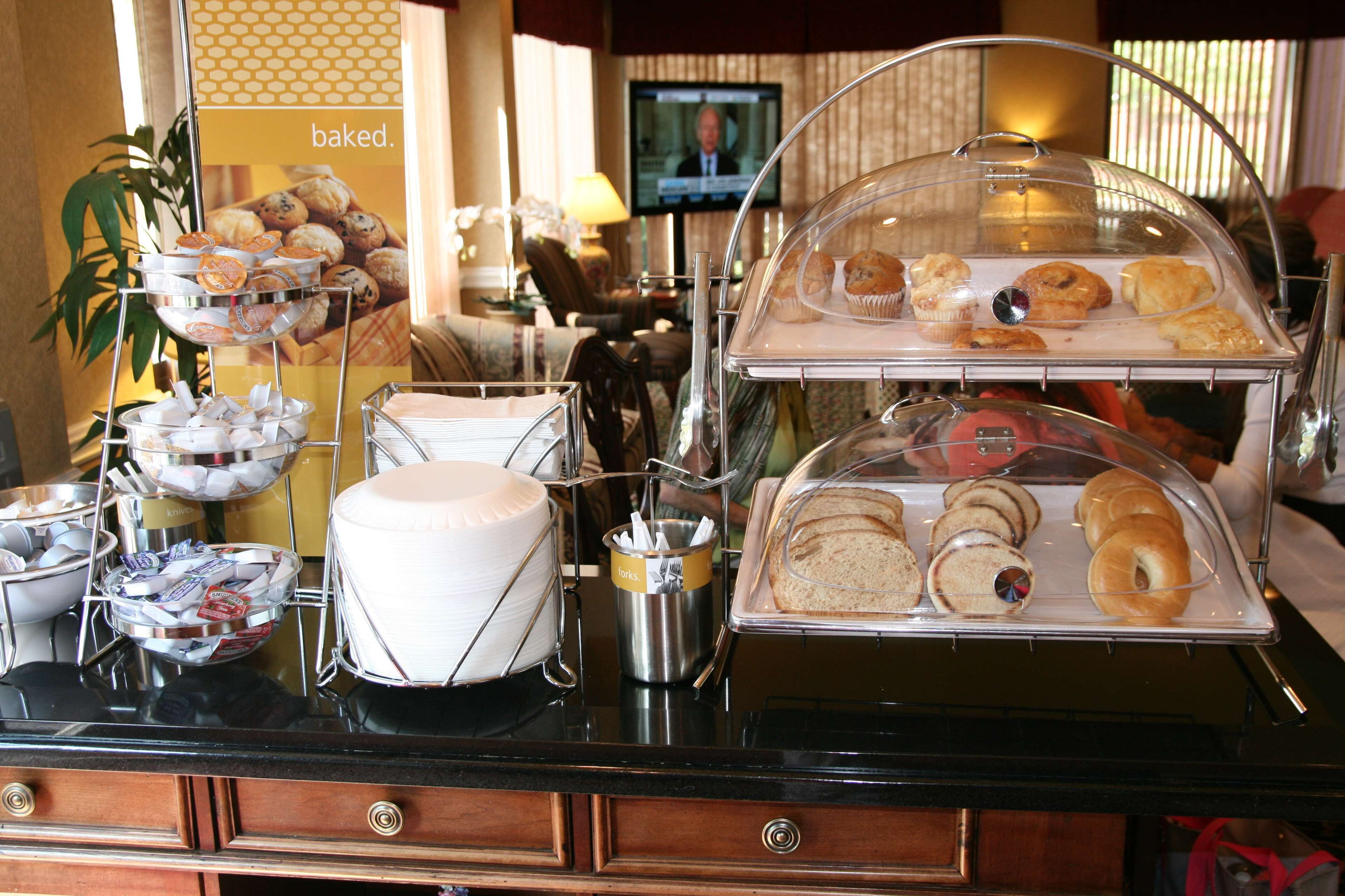A buffet with various baked goods, including pastries and bread, displayed on a counter with a television in the background.