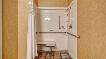 Un petit espace de douche fermé, doté d’un banc, de barres d’appui et d’un pommeau de douche.