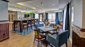 A hotel dining area with wooden flooring, a central table with chairs, and blue upholstered seating.