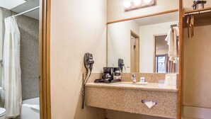 A bathroom with a granite countertop, a hairdryer, a coffee maker, and a mirror with lights.