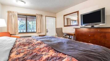 A hotel room with a bed, a desk, a television, and a window with curtains.