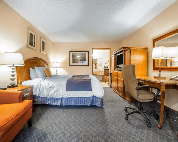 A hotel room with a bed, desk, chair, dresser, and a television.