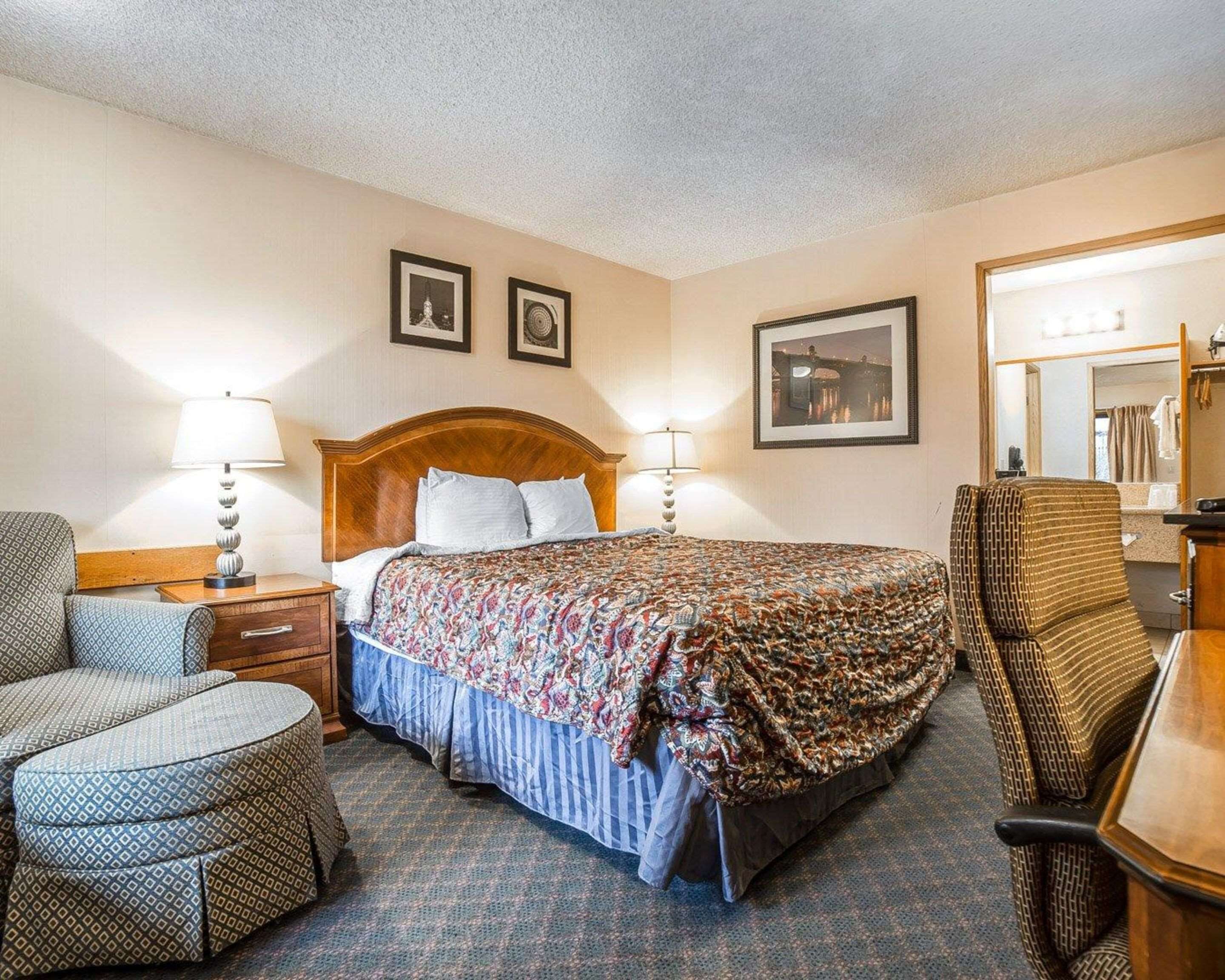 A hotel room with a bed, two bedside tables, a chair, a desk, a mirror, and framed pictures on the wall.