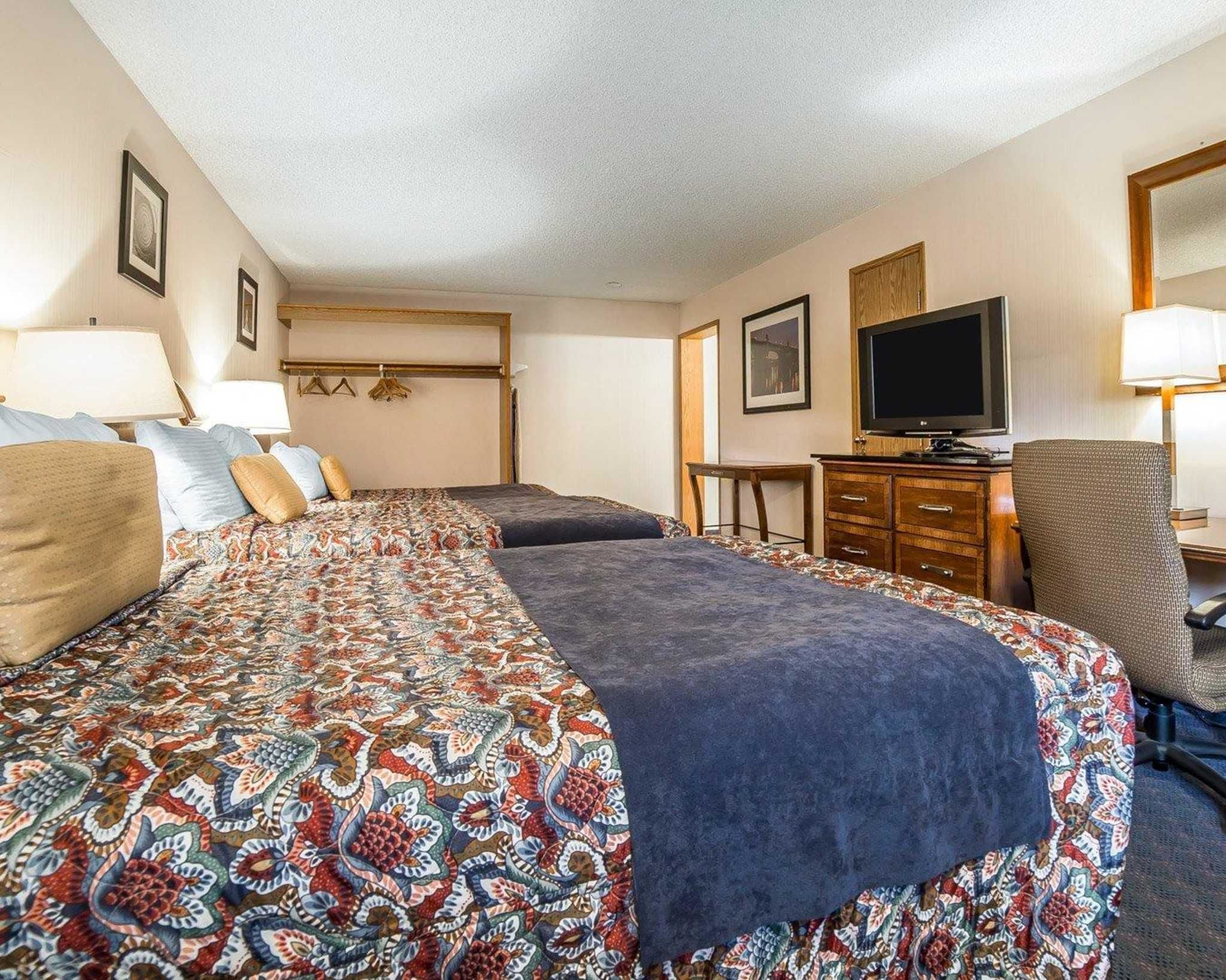 A hotel room with two beds, a television, a desk, and a chair.