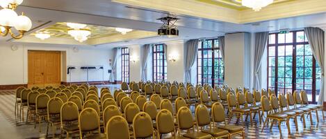 A conference room with rows of chairs, large windows, and chandeliers.