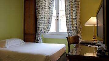 Una camera d'albergo con un letto, una sedia, una scrivania con una lampada e una televisione.