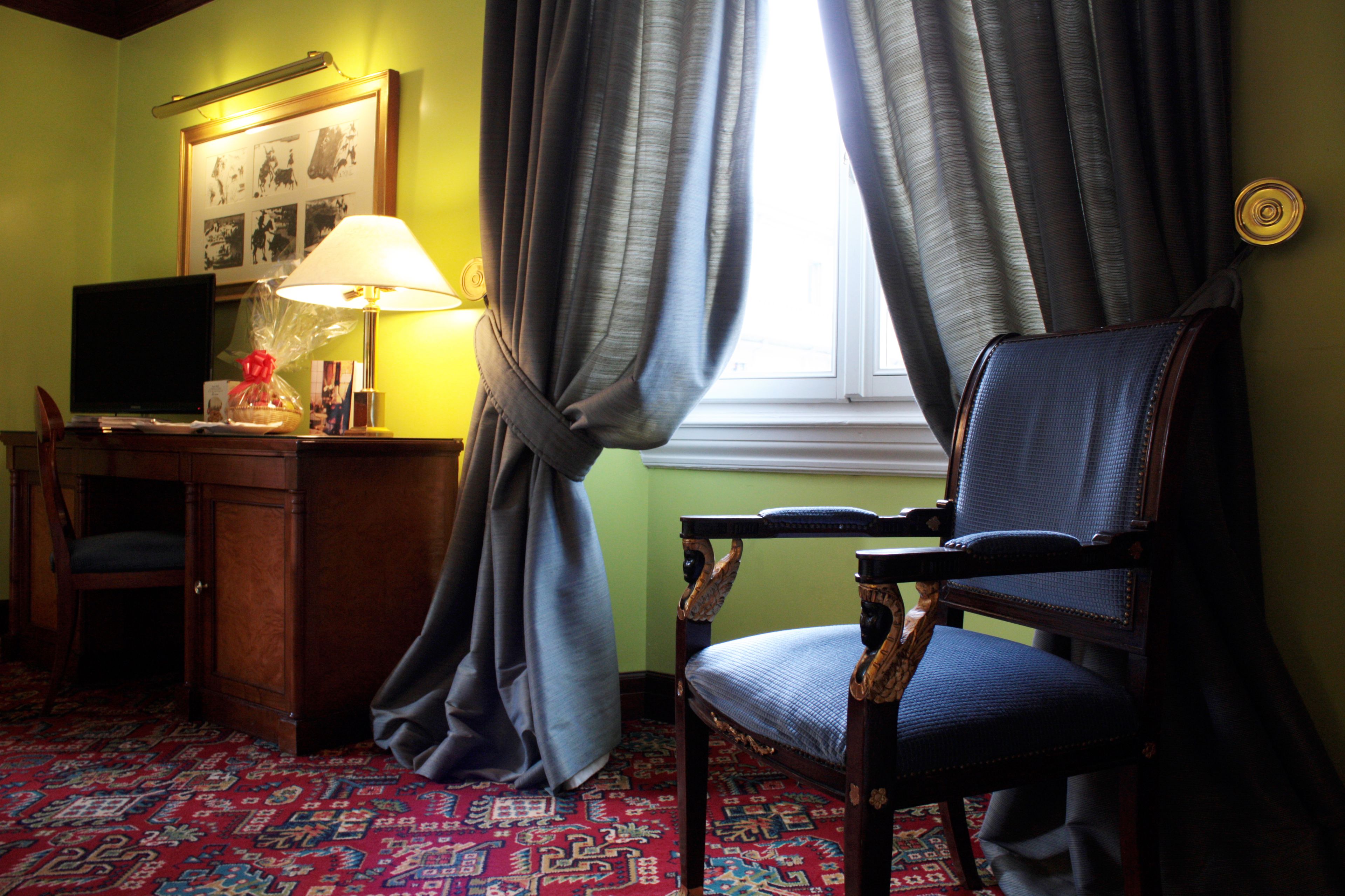 A room with a desk, chair, lamp, and a window with curtains.