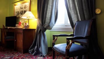 A room with a desk, chair, lamp, and a window with curtains.