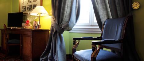 A room with a desk, chair, lamp, and a window with curtains.