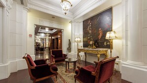 Un hall con tres sillones de terciopelo rojo, una mesa de centro de mármol y un cuadro grande en la pared.