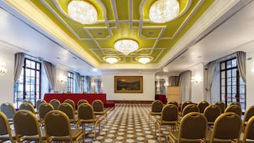 A conference room with a checkered floor, rows of chairs, a red podium, and chandeliers.