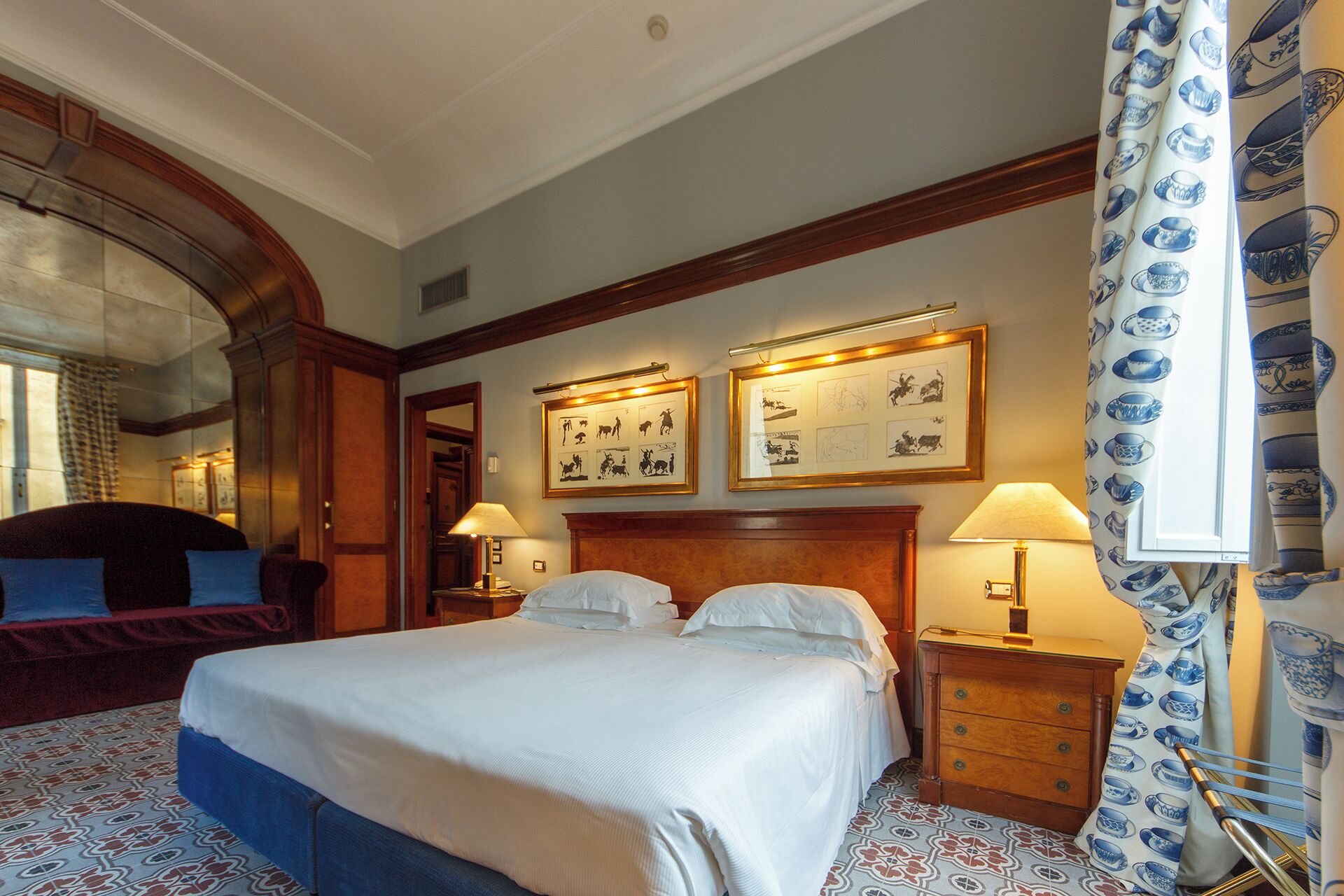 A hotel room with a large bed, two bedside tables with lamps, a wooden headboard, and two framed pictures on the wall.
