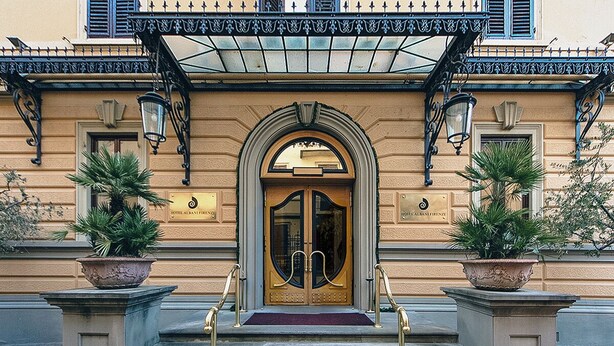 Entrada de hotel con puertas dobles, toldo y dos macetas a cada lado.