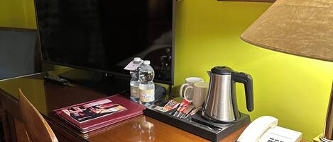 A hotel room with a wooden desk, a television, a coffee maker, a telephone, and a lamp.