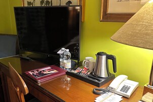 A hotel room with a wooden desk, a television, a coffee maker, a telephone, and a lamp.