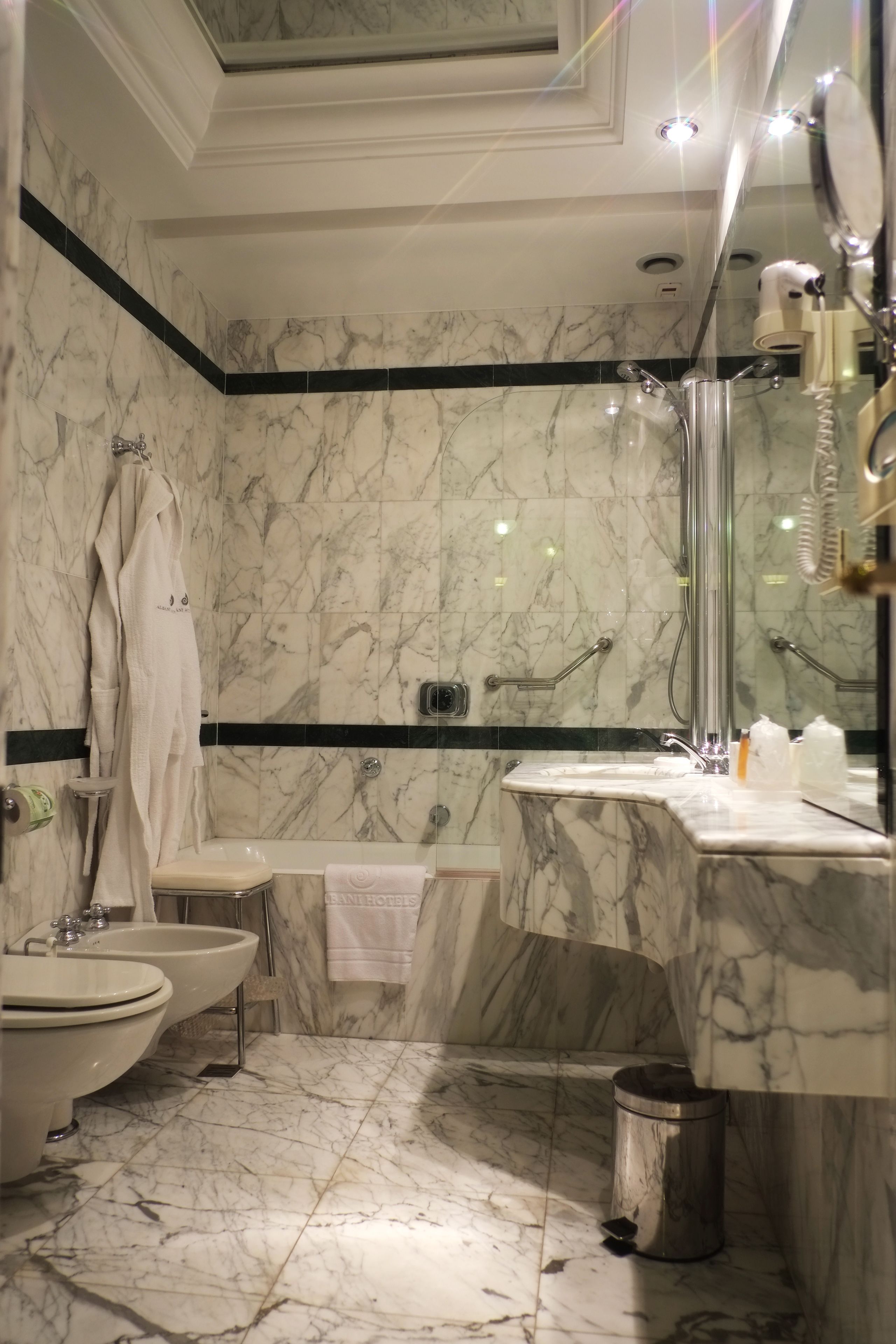 A bathroom with marble walls, a bidet, a toilet, a sink, and a shower.
