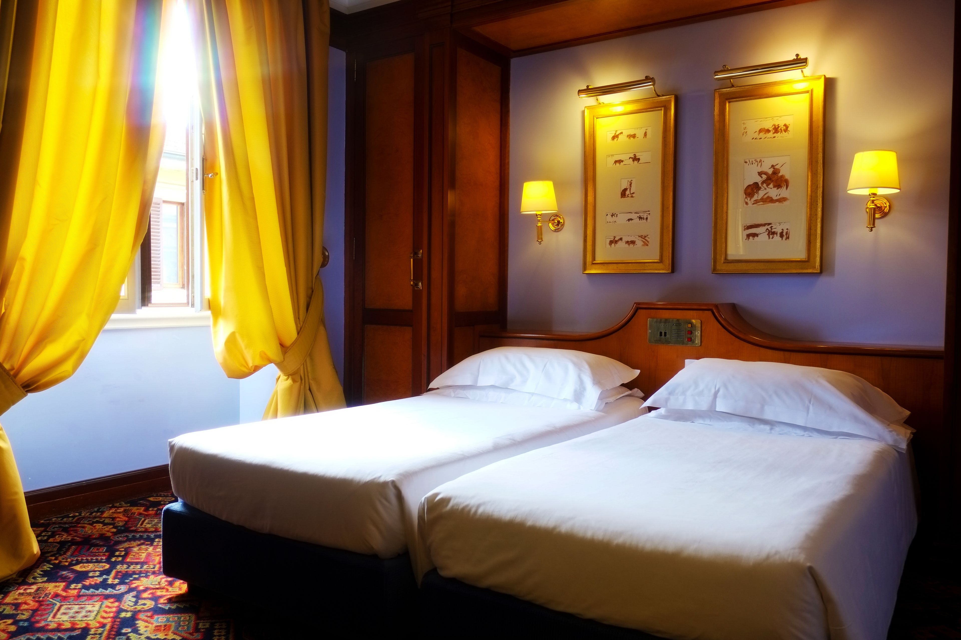 A hotel room with two beds, a patterned carpet, and wall-mounted lamps.