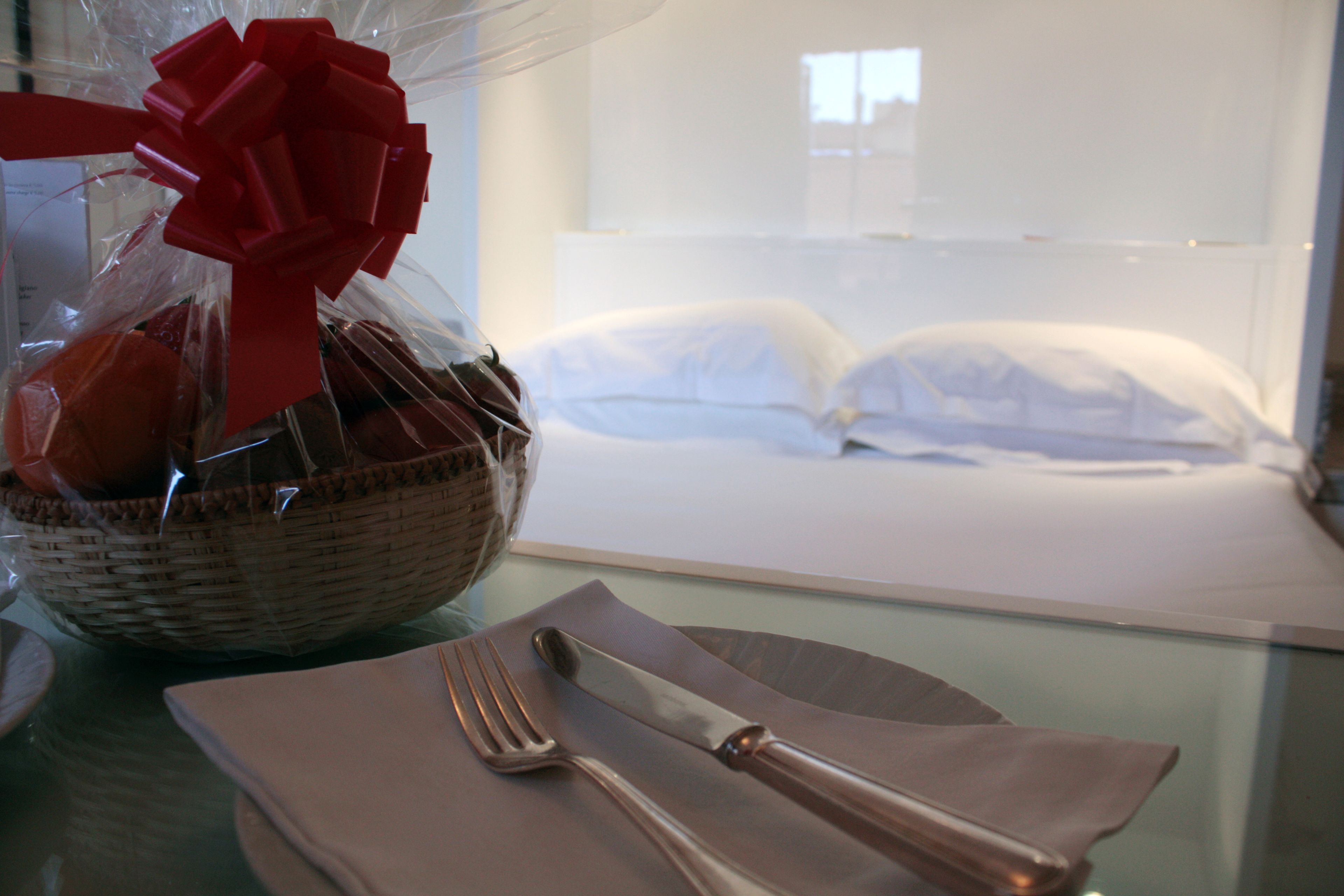 A neatly arranged breakfast setting with a basket of pastries, a red bow, and a bed in the background.