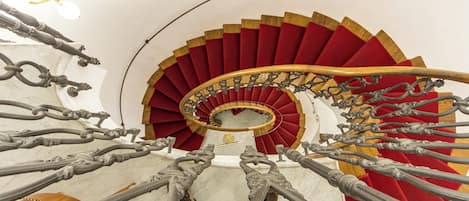 A spiral staircase with red steps and a white wall.