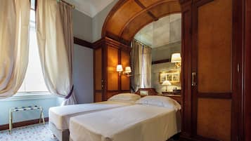Una habitación de hotel con dos camas, un armario de madera, un espejo y una mesita.