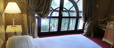 A hotel room with a large bed, a nightstand with a lamp, a chair, and a window with curtains.