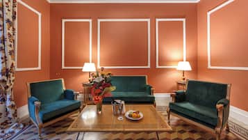 Una habitación con dos sofás verdes, una mesa de centro con fruta y dos lámparas.